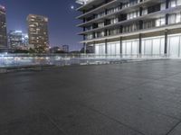 a skate board sitting on top of a concrete floor near tall buildings at night as seen from a sidewalk