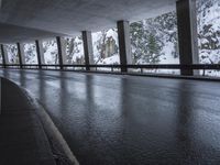 a person riding a skate board on top of a frozen street beneath a bridge over a snowy mountain