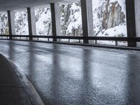 a person riding a skate board on top of a frozen street beneath a bridge over a snowy mountain