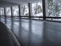 a person riding a skate board on top of a frozen street beneath a bridge over a snowy mountain