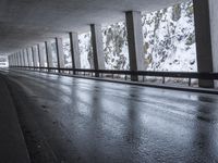 a person riding a skate board on top of a frozen street beneath a bridge over a snowy mountain