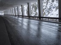 a person riding a skate board on top of a frozen street beneath a bridge over a snowy mountain