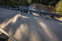 a skateboard sits on top of a railing over a river near a sidewalk and a walkway