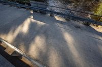 a skateboard sits on top of a railing over a river near a sidewalk and a walkway