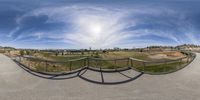 a 360 - camera photo taken from a skateboard ramp at an outdoor park with cityscape in the distance