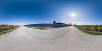 a fisheye view of the sun over a half - pipe skateboard park near an area with green grass and bushes