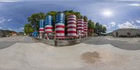 an empty skateboard park with many colored cylinders sticking out of the ground and trees in the background