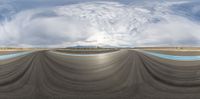 a panoramic lens of a skateboard park in a cloud filled sky and with a person doing a trick