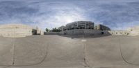 a skateboard park in a city with buildings and blue skies in the background with some clouds