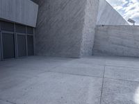 a person riding a skateboard on the sidewalk in front of a building with concrete walls