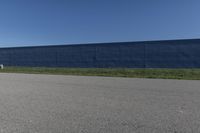 the skateboard is standing alone in a parking lot with a fence on one side and blue covering the opposite wall