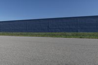 the skateboard is standing alone in a parking lot with a fence on one side and blue covering the opposite wall