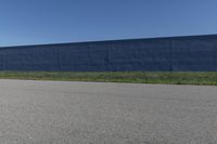 the skateboard is standing alone in a parking lot with a fence on one side and blue covering the opposite wall