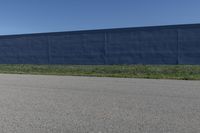 the skateboard is standing alone in a parking lot with a fence on one side and blue covering the opposite wall