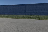 the skateboard is standing alone in a parking lot with a fence on one side and blue covering the opposite wall