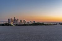 a skateboarder is riding on the asphalt near city skylines in background at sunset