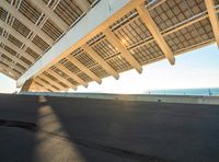 a skate boarder riding underneath the sun - streaked structure of a bridge at sunset