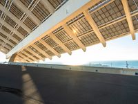a skate boarder riding underneath the sun - streaked structure of a bridge at sunset