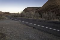 a skateboarder on a dirt road in the desert during sunset time, looking at a rocky hill and horizon