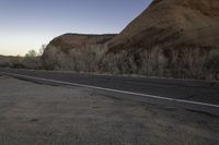 a skateboarder on a dirt road in the desert during sunset time, looking at a rocky hill and horizon