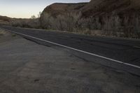 a skateboarder on a dirt road in the desert during sunset time, looking at a rocky hill and horizon