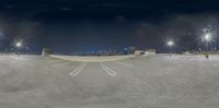 a skateboarder stands in an empty parking lot at night time with cityscape in the background