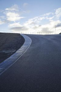 a lone skateboarder riding a bike on a hilly road in the sun with grass and trees