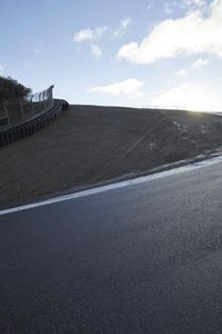 a lone skateboarder riding a bike on a hilly road in the sun with grass and trees