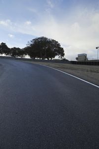 a lone skateboarder riding a bike on a hilly road in the sun with grass and trees