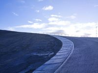 a lone skateboarder riding a bike on a hilly road in the sun with grass and trees