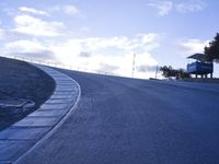a lone skateboarder riding a bike on a hilly road in the sun with grass and trees