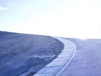 a lone skateboarder riding a bike on a hilly road in the sun with grass and trees