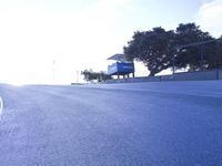 a lone skateboarder riding a bike on a hilly road in the sun with grass and trees