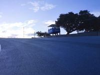 a lone skateboarder riding a bike on a hilly road in the sun with grass and trees