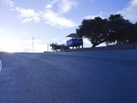 a lone skateboarder riding a bike on a hilly road in the sun with grass and trees