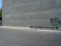 the skateboarder is jumping in front of a cement wall and fence with graffiti