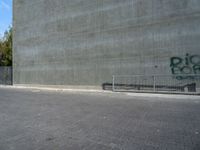 the skateboarder is jumping in front of a cement wall and fence with graffiti