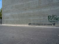 the skateboarder is jumping in front of a cement wall and fence with graffiti