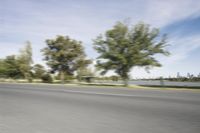 a skateboarder riding down the road with a city in the background and green trees and grass