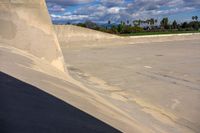 skateboarder performing trick on large cement ramp in urban area under blue skies with clouds