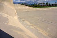 skateboarder performing trick on large cement ramp in urban area under blue skies with clouds