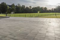 a skateboarder performs a trick on an empty brick area at the edge of a tennis court