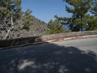 a skateboarder rides on a small paved road near the mountainside in front of some trees