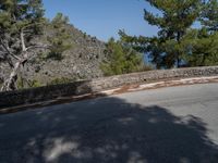 a skateboarder rides on a small paved road near the mountainside in front of some trees