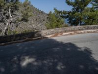 a skateboarder rides on a small paved road near the mountainside in front of some trees