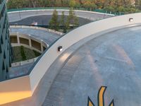 a skateboarder rides on the ramp in a curve shaped ramp between two large buildings and a mountain in the background