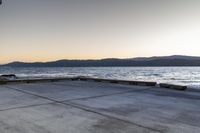 a skate boarder riding on an empty road near the water and mountain range in the distance