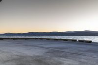 a skate boarder riding on an empty road near the water and mountain range in the distance