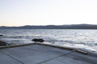 a skate boarder riding on an empty road near the water and mountain range in the distance