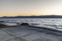 a skate boarder riding on an empty road near the water and mountain range in the distance